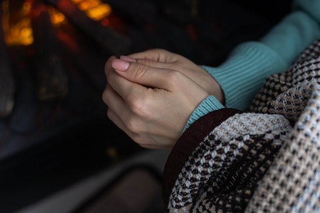 Woman warming cold hands near a fireplace, illustrating poor circulation or low oxygen delivery after age 50