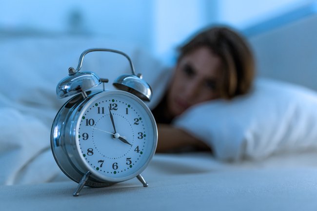 Woman lying awake at night looking at alarm clock during insomnia episode related to magnesium for sleep
