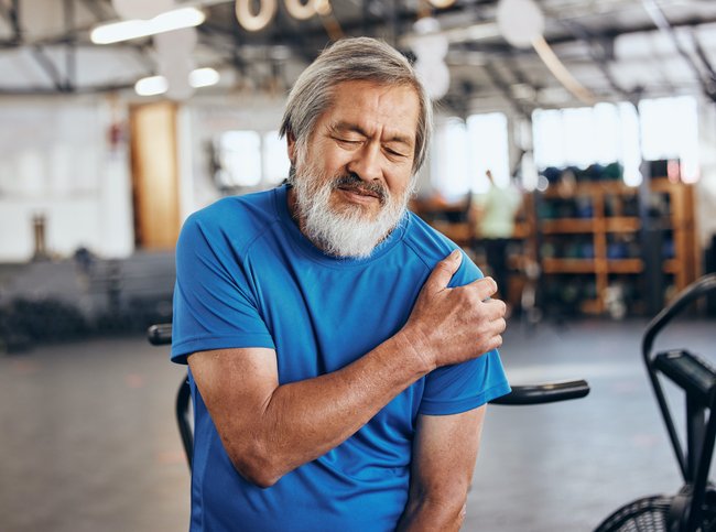 Older man holding shoulder in pain at gym illustrating muscle cramps and tightness