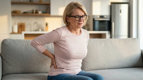 Woman sitting on a couch holding her lower back in pain, illustrating inflammation and joint discomfort in the body.