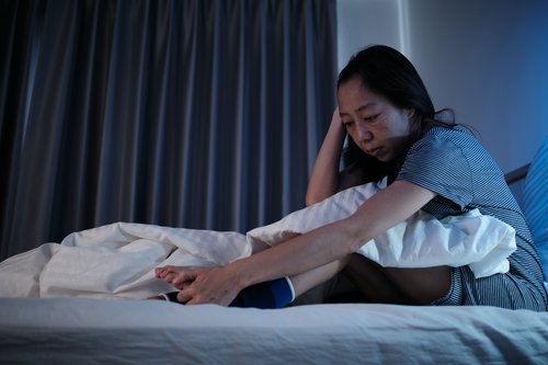 Woman sitting up in bed at night holding her leg due to discomfort or cramping