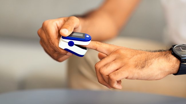 Person using a pulse oximeter on finger to check oxygen saturation levels at home