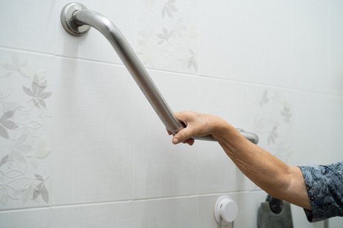 Senior using a grab bar in bathroom for stability and fall prevention. Slippery surfaces are one of the top causes of falls in senior adults.