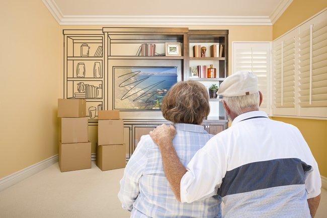 Senior couple sitting together in a room with moving boxes, preparing for moving and relocating.