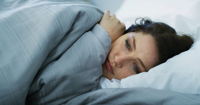 Woman lying awake in bed at night experiencing discomfort or symptoms that feel worse after dark